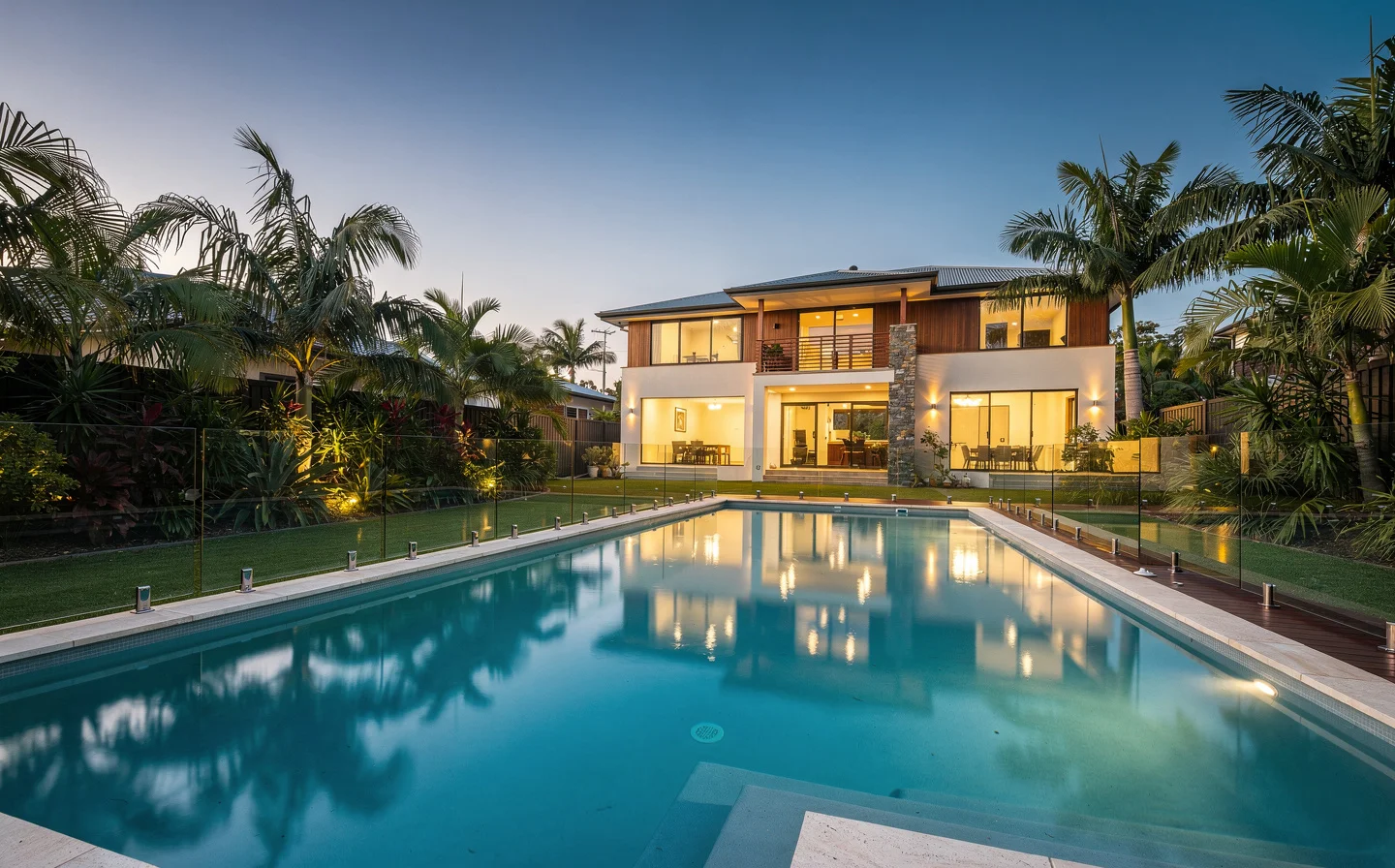 A finished concrete pool at dusk in a Sunshine Coast backyard, calm water and warm lighting